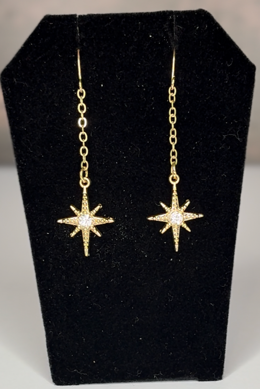 Gold star-shaped earrings on a black jewelry display stand.